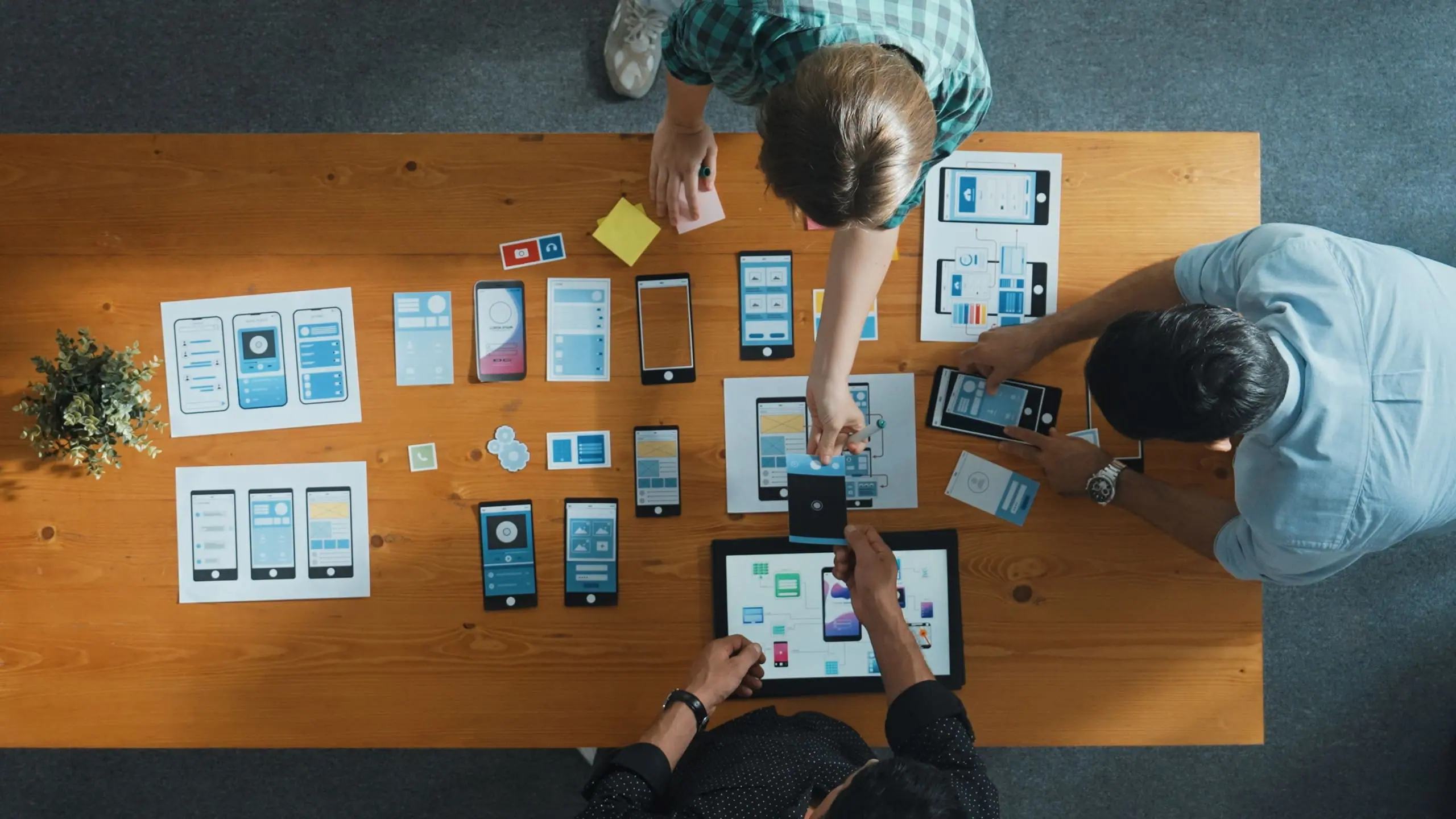 A product team arranging mobile app wireframes and prototypes on a table during a design workshop.