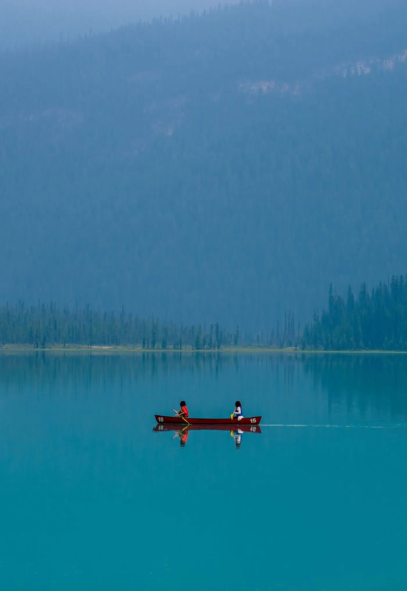 A red canoe gliding across the still, emerald water of a mountain lake in the Canadian Rockies.
